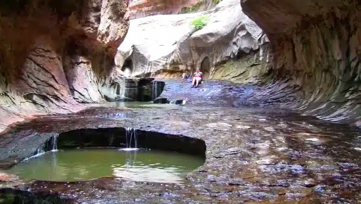 A secluded rocky cave with a small pool of water and a person sitting on the edge.